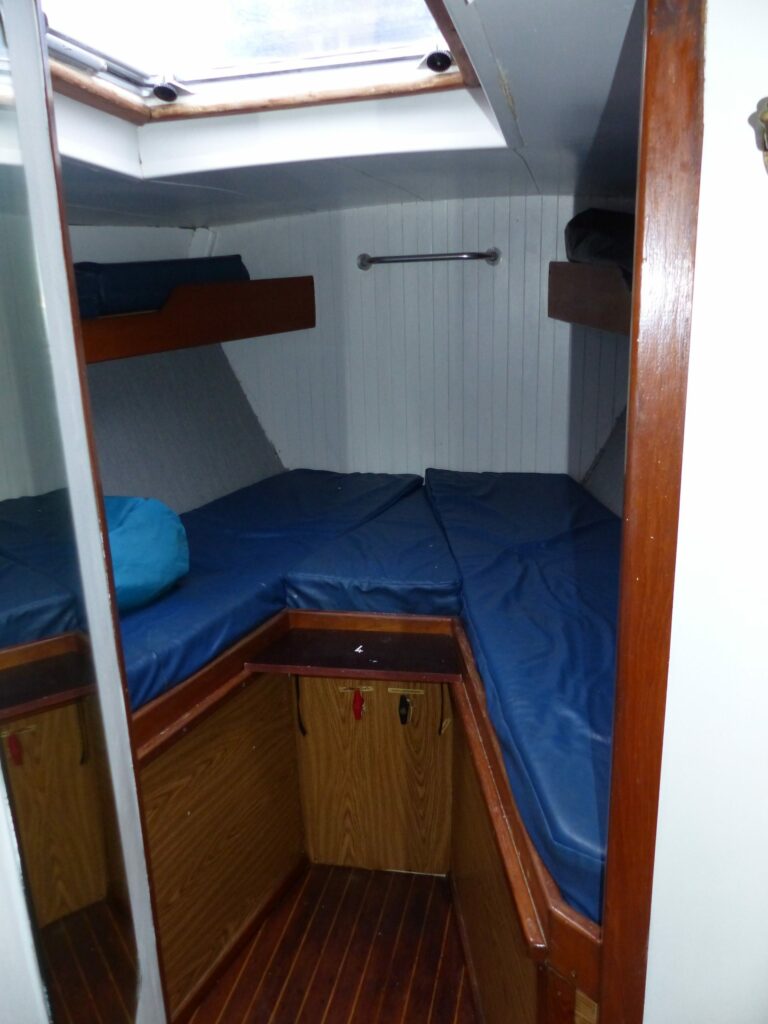 Une cabine à deux couchettes avec ses matelas bleus, sous le hublot de pont