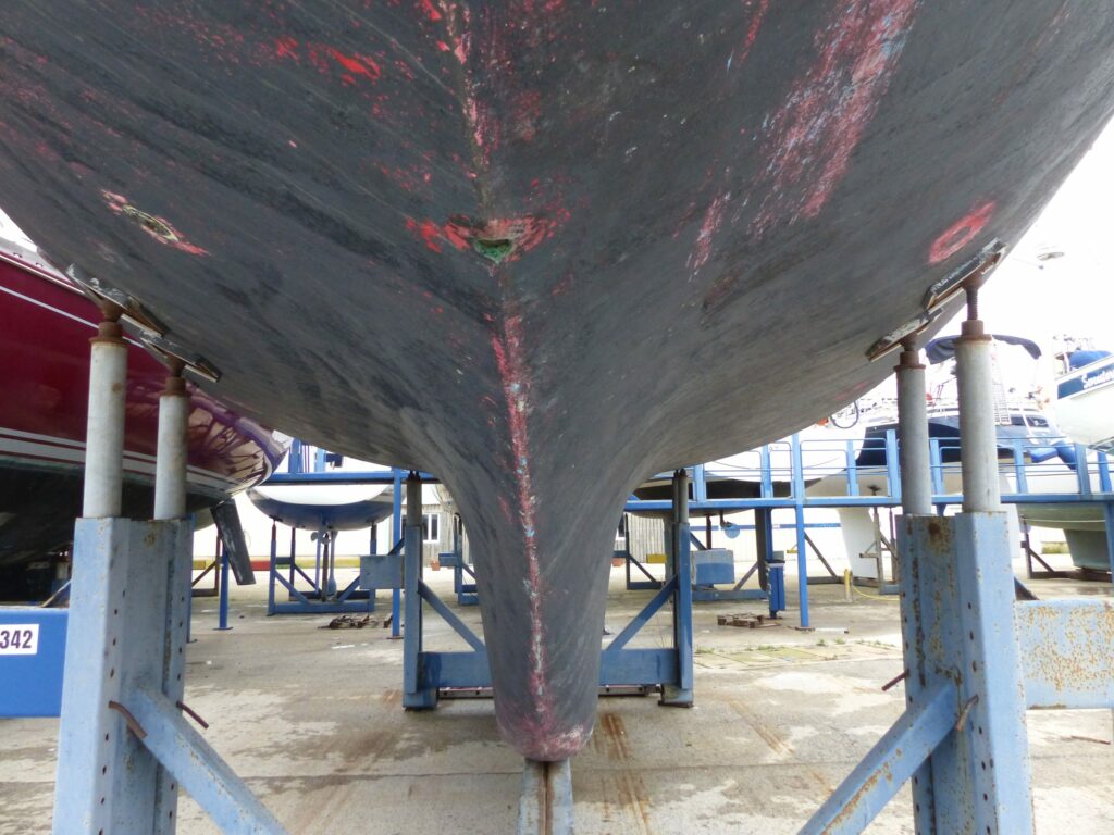 L’étrave et la quille du CQS Evidence au sec sur son ber, carène couverte d’antifouling rouge