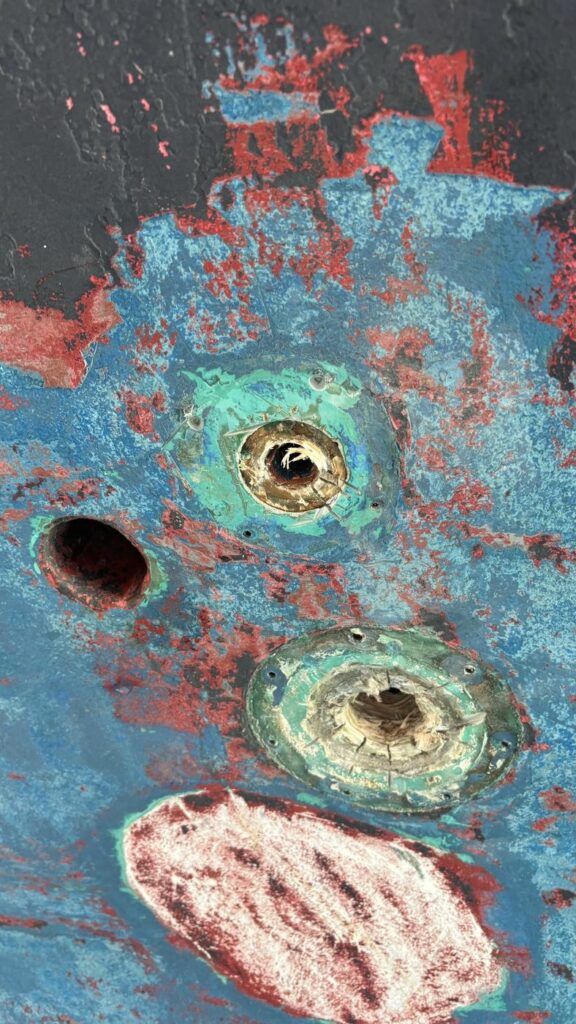 Gros plan sur deux passe-coques en laiton corrodés, la peinture grattée tout autour