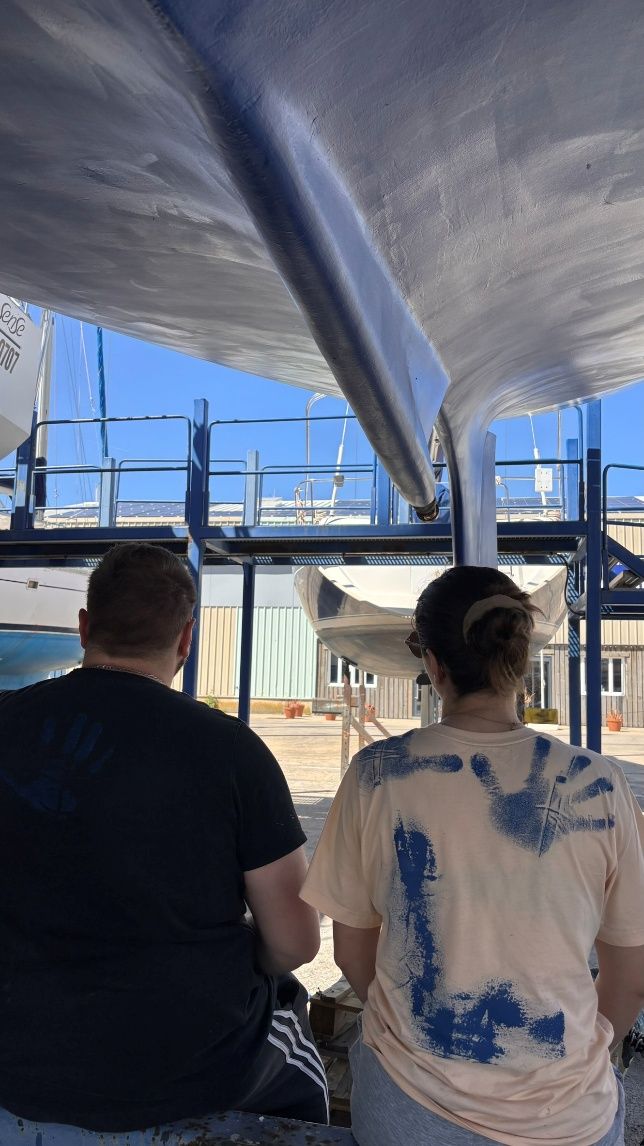 Rémi et Léa sous la coque du CQS Evidence, les mains et les tee-shirts pleins de peinture bleue
